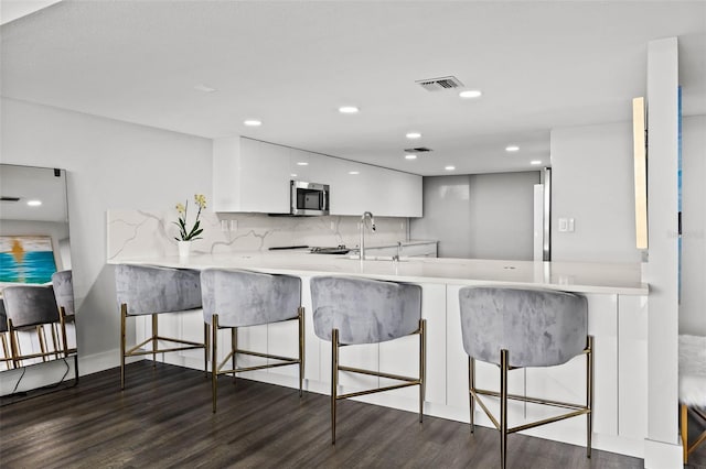 kitchen with kitchen peninsula, dark hardwood / wood-style floors, tasteful backsplash, white cabinetry, and a breakfast bar area