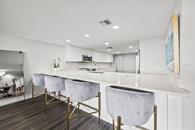 kitchen with a breakfast bar area, kitchen peninsula, white cabinetry, and dark hardwood / wood-style flooring