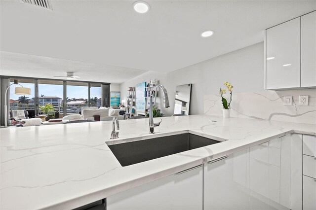 kitchen with kitchen peninsula, light stone counters, sink, and white cabinets