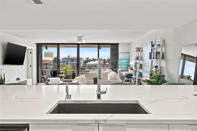 kitchen with ceiling fan, light stone counters, white cabinetry, and sink