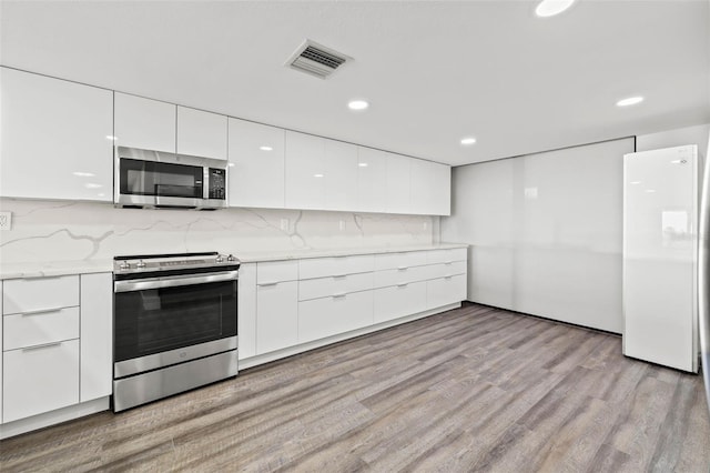 kitchen featuring backsplash, light stone countertops, light wood-type flooring, white cabinetry, and stainless steel appliances