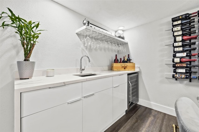 bar featuring dark wood-type flooring, sink, light stone counters, white cabinetry, and beverage cooler