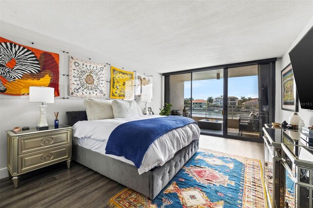 bedroom featuring access to exterior, a textured ceiling, expansive windows, and dark wood-type flooring