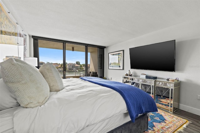 bedroom with a textured ceiling, a wall of windows, dark wood-type flooring, and access to outside