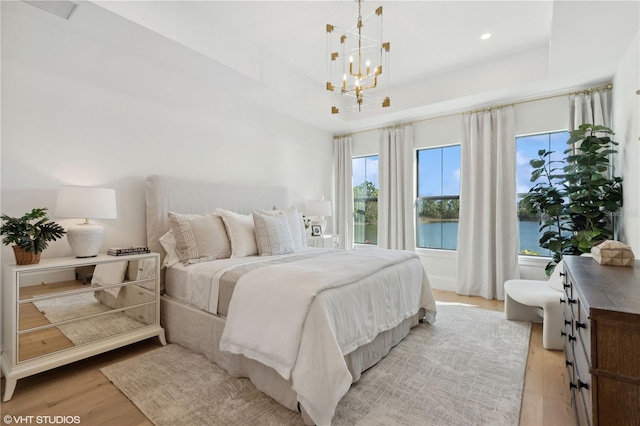 bedroom with a water view, a notable chandelier, and light wood-type flooring