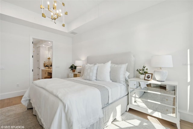 bedroom featuring ensuite bathroom, light hardwood / wood-style flooring, and a notable chandelier