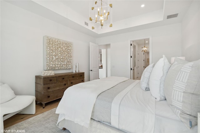 bedroom with a chandelier, ensuite bath, a tray ceiling, and light hardwood / wood-style flooring