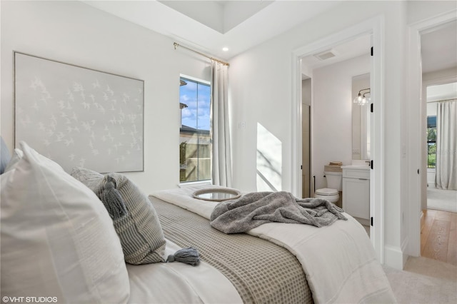 bedroom with ensuite bath, hardwood / wood-style floors, and multiple windows