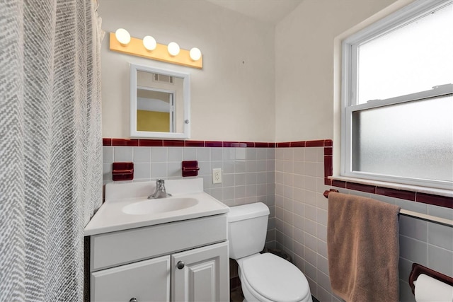 bathroom with vanity, toilet, and tile walls