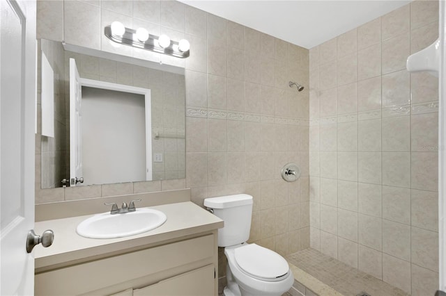 bathroom with a tile shower, vanity, tile walls, and toilet