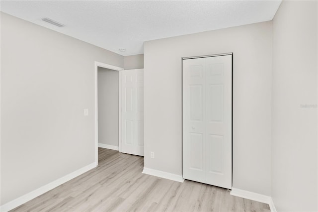 unfurnished bedroom featuring light hardwood / wood-style floors, a textured ceiling, and a closet