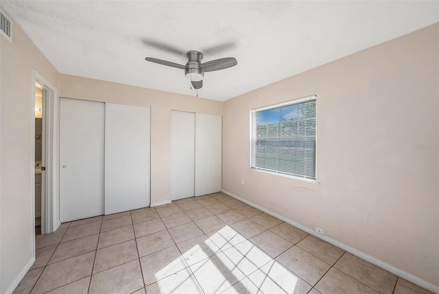 unfurnished bedroom with ceiling fan, light tile patterned floors, a textured ceiling, and multiple closets