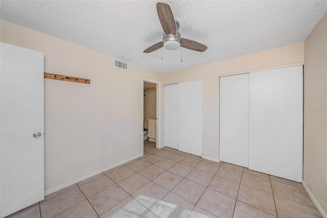 unfurnished bedroom with multiple closets, ceiling fan, light tile patterned floors, and a textured ceiling