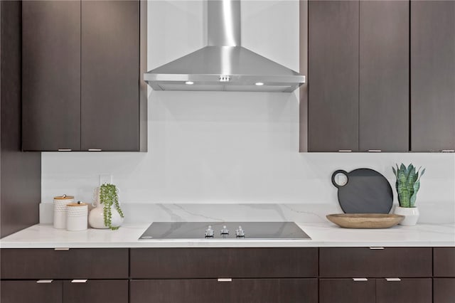 kitchen with light stone countertops, black electric stovetop, dark brown cabinetry, and wall chimney exhaust hood