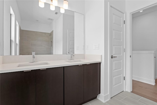 full bath featuring tiled shower, a sink, visible vents, and double vanity