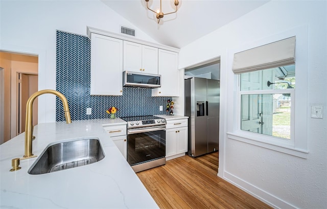 kitchen with white cabinets, appliances with stainless steel finishes, sink, and lofted ceiling