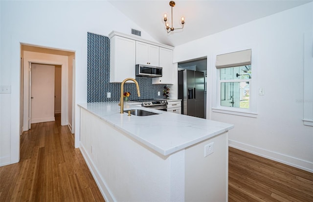 kitchen with appliances with stainless steel finishes, decorative light fixtures, white cabinetry, sink, and kitchen peninsula