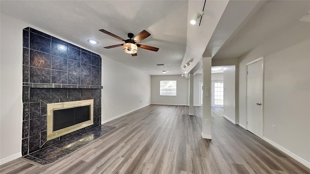 unfurnished living room with a fireplace, wood-type flooring, a textured ceiling, and ceiling fan