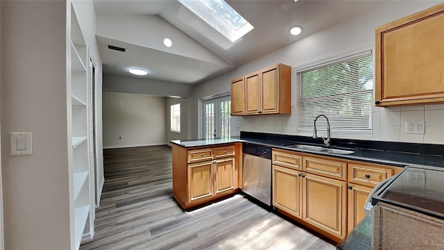 kitchen featuring backsplash, sink, vaulted ceiling with skylight, stainless steel dishwasher, and kitchen peninsula