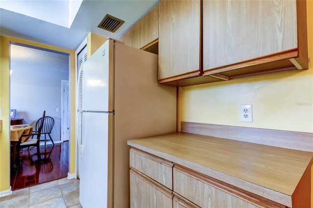 kitchen with light tile patterned floors, light brown cabinets, and white refrigerator