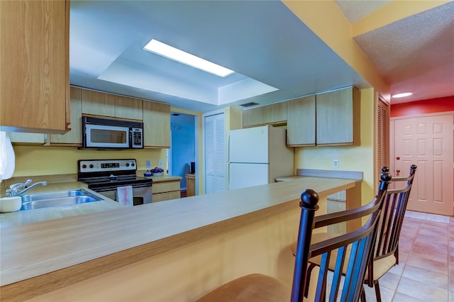 kitchen with sink, stainless steel appliances, a raised ceiling, kitchen peninsula, and light tile patterned floors