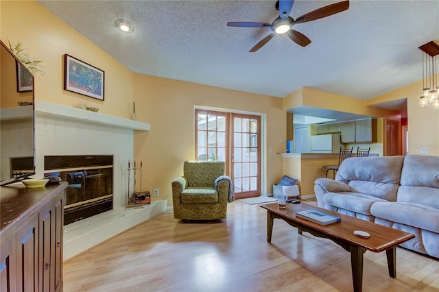 living room with vaulted ceiling, ceiling fan, light hardwood / wood-style floors, and a textured ceiling