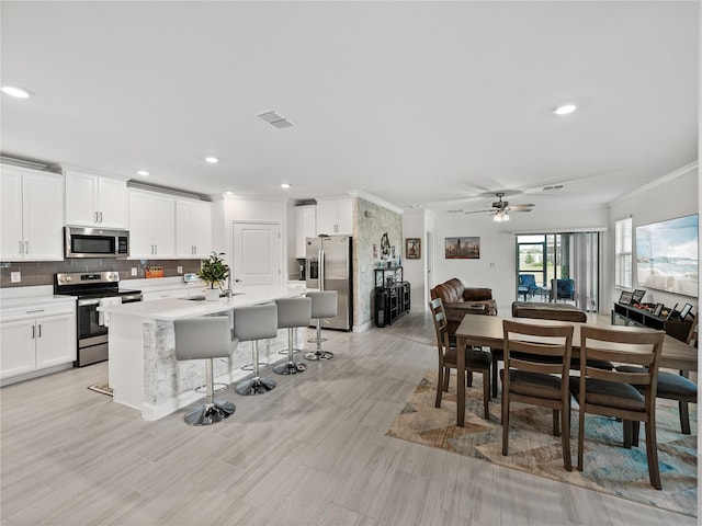 interior space with ceiling fan, an island with sink, a breakfast bar, white cabinets, and appliances with stainless steel finishes