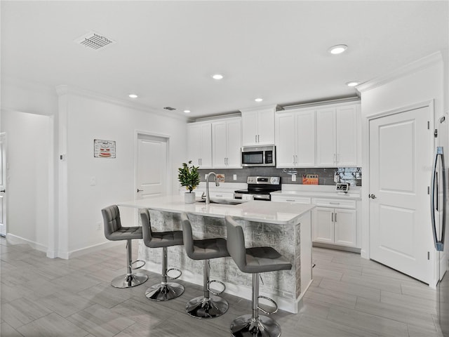 kitchen with white cabinetry, sink, stainless steel appliances, an island with sink, and a kitchen bar