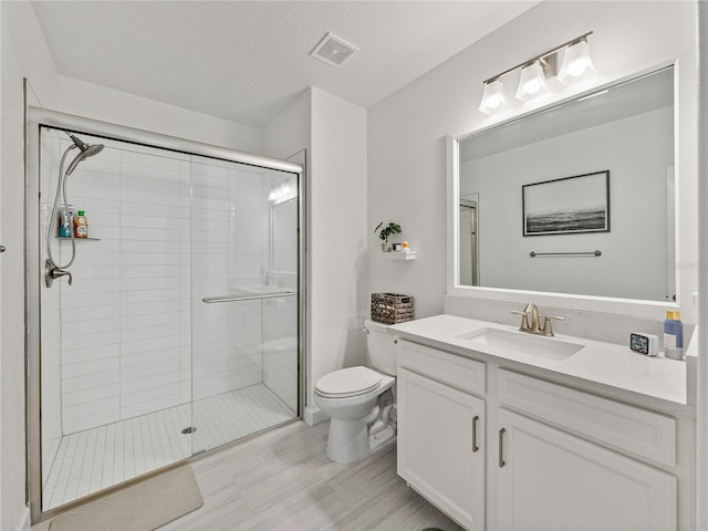 bathroom featuring vanity, toilet, a shower with door, and a textured ceiling