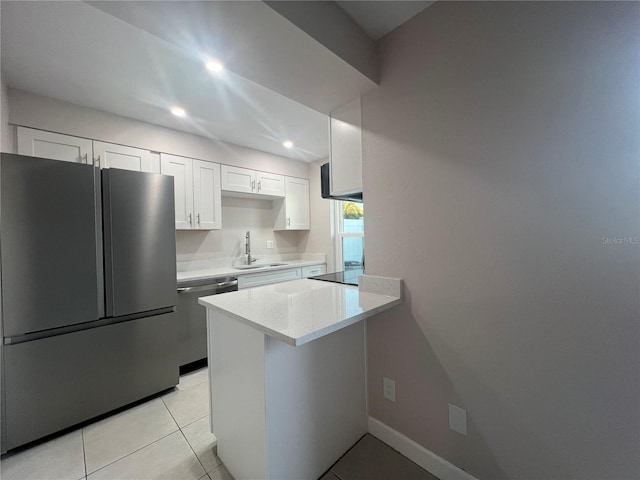 kitchen with kitchen peninsula, appliances with stainless steel finishes, sink, light tile patterned floors, and white cabinetry