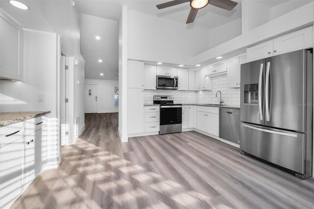 kitchen featuring light stone countertops, stainless steel appliances, light hardwood / wood-style flooring, high vaulted ceiling, and white cabinets