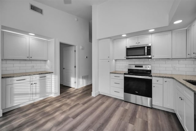 kitchen featuring hardwood / wood-style floors, white cabinets, a high ceiling, and appliances with stainless steel finishes