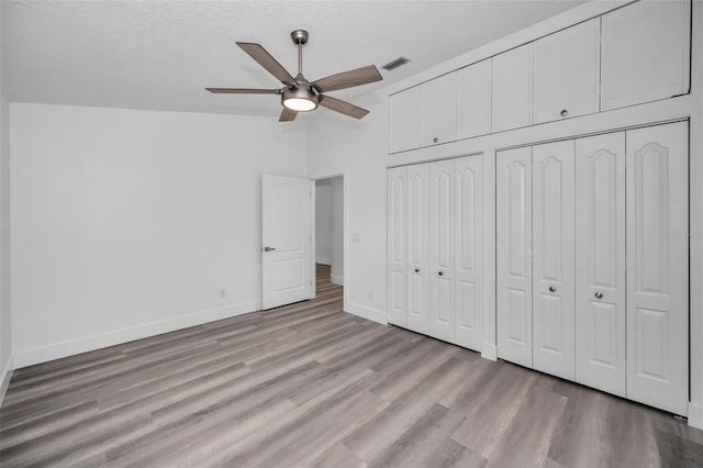 unfurnished bedroom featuring lofted ceiling, light wood-type flooring, ceiling fan, and multiple closets