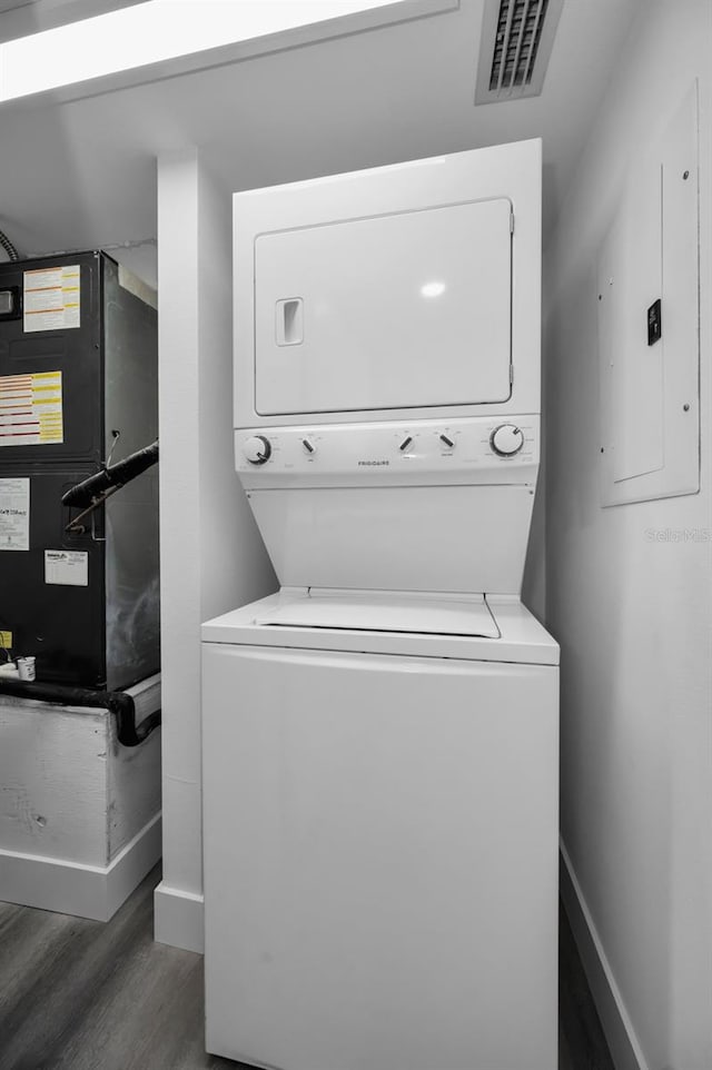 laundry room featuring electric panel, stacked washer and dryer, and dark hardwood / wood-style floors