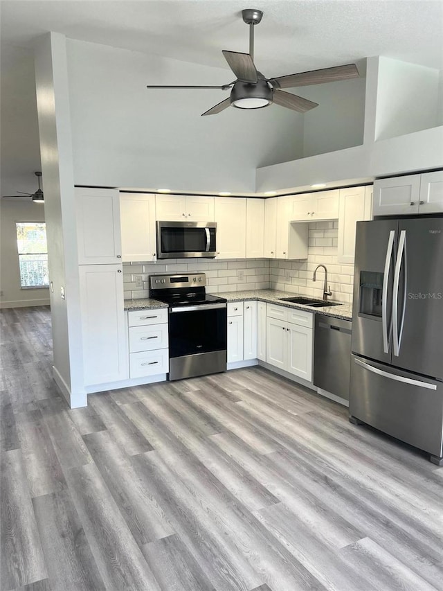 kitchen featuring light wood-type flooring, stainless steel appliances, sink, high vaulted ceiling, and white cabinetry