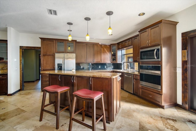 kitchen featuring a kitchen island, appliances with stainless steel finishes, pendant lighting, decorative backsplash, and light stone countertops