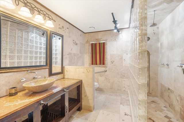 bathroom featuring a tile shower, tile walls, vanity, toilet, and crown molding