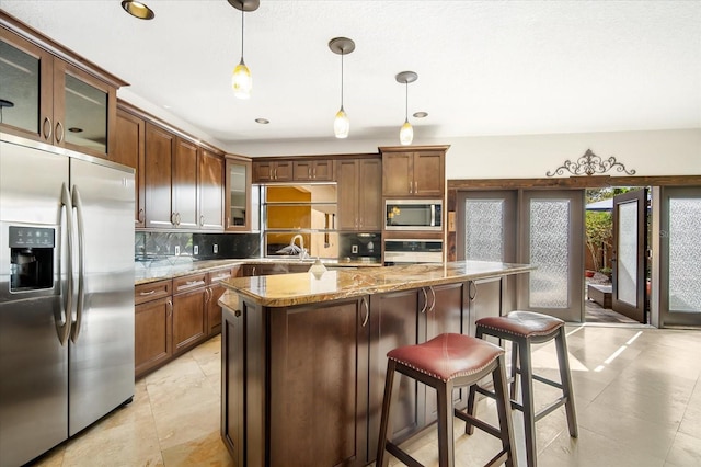 kitchen with pendant lighting, appliances with stainless steel finishes, backsplash, a center island, and light stone counters