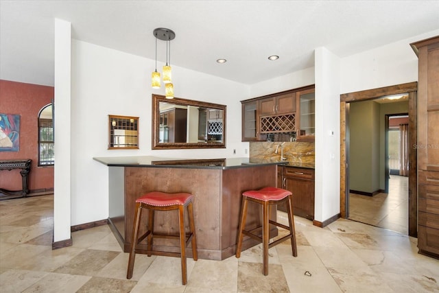 kitchen with sink, a breakfast bar, hanging light fixtures, backsplash, and kitchen peninsula