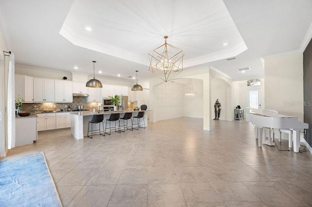 kitchen featuring a raised ceiling, decorative light fixtures, white cabinetry, and an island with sink