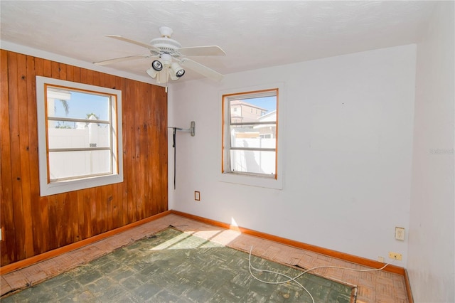 empty room with plenty of natural light, ceiling fan, and wooden walls