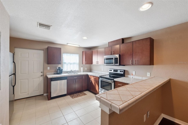 4148 Rudder Way, New Port Richey, FL 34652 - kitchen with stainless steel appliances, a peninsula, tile counters, a sink, and a textured ceiling
