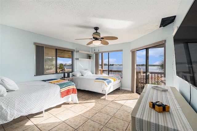 tiled bedroom featuring access to outside, ceiling fan, a water view, and a textured ceiling