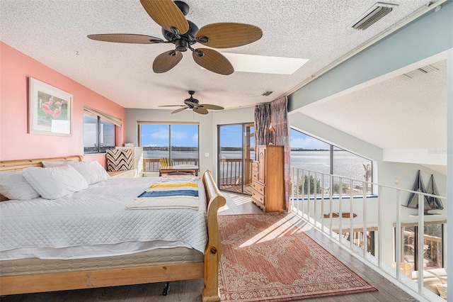 bedroom with a skylight, ceiling fan, wood-type flooring, a textured ceiling, and access to outside