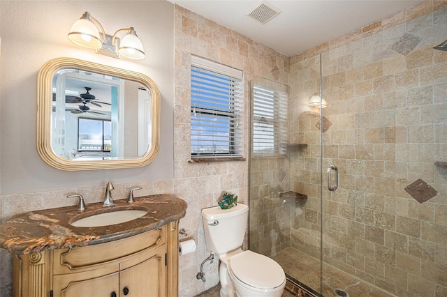 bathroom with ceiling fan, walk in shower, toilet, vanity, and tile walls