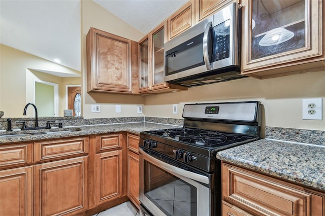 kitchen with stone counters, sink, a textured ceiling, vaulted ceiling, and appliances with stainless steel finishes