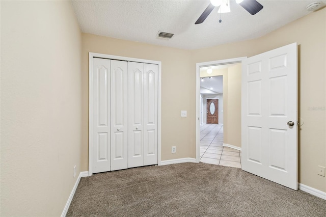 unfurnished bedroom featuring ceiling fan, a closet, light colored carpet, and a textured ceiling