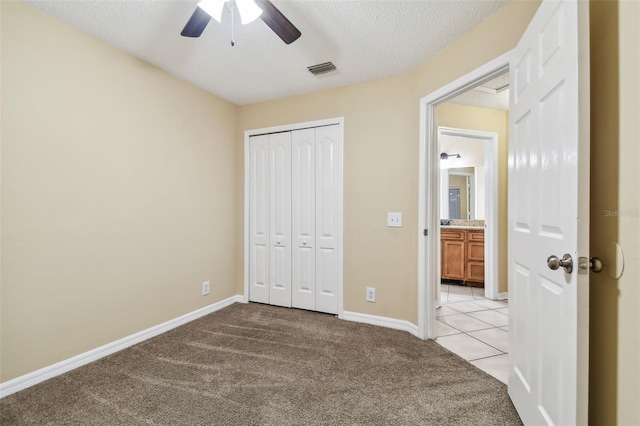 unfurnished bedroom with ceiling fan, a closet, light colored carpet, and a textured ceiling