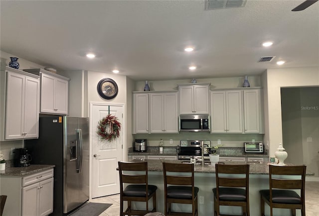 kitchen with dark stone countertops, light tile patterned floors, stainless steel appliances, and a breakfast bar area