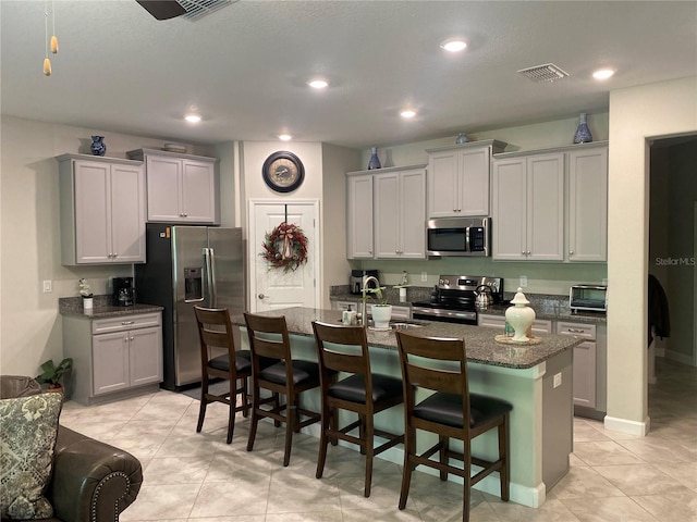 kitchen with a kitchen breakfast bar, stainless steel appliances, a kitchen island with sink, and gray cabinetry